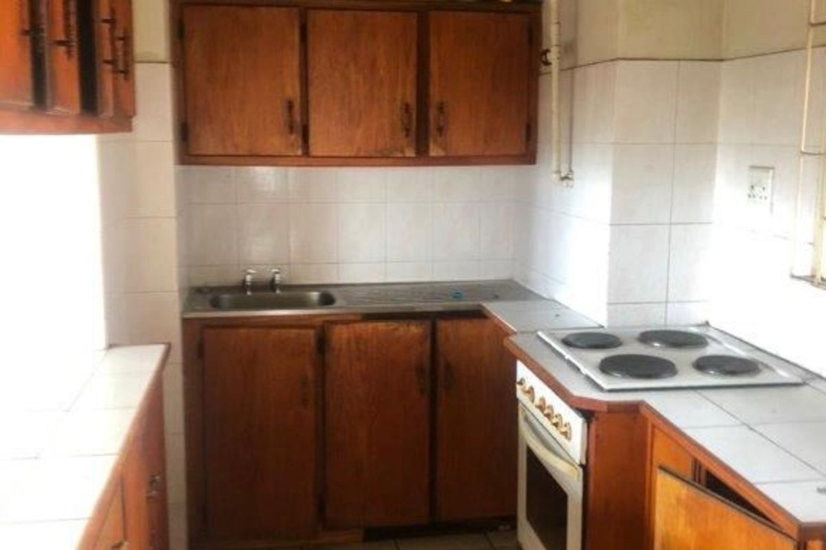 A dated kitchen featuring wooden cabinetry, tiled surfaces, and built-in cooking appliances, offering significant potential for a modern renovation.