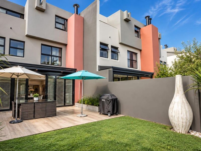 A well-maintained rear exterior featuring a tiled patio area, landscaped garden, and modern multi-story townhouse facade with sliding glass doors.