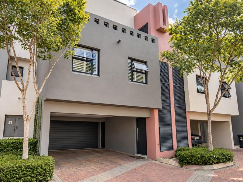 Modern multi-story townhouse facade featuring a paved driveway, integrated garage, and contemporary architectural detailing with contrasting grey and pink exterior finishes.