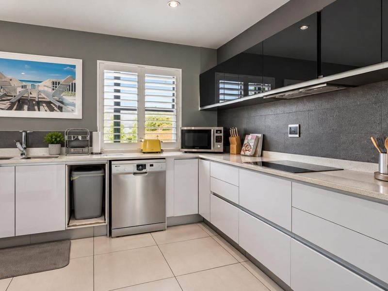 Modern kitchen featuring sleek white and black cabinetry, stone countertops, induction hob, integrated extractor, and tiled flooring with plantation shutters.