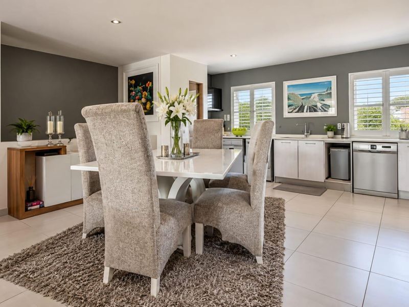 A bright open-plan living and dining area featuring modern cabinetry, integrated appliances, tiled flooring, and plantation shutters, creating a functional and cohesive space.