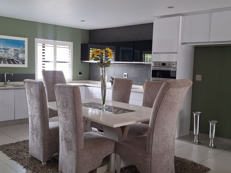 Open-plan kitchen and dining area featuring modern white cabinetry, integrated oven, tiled flooring, and plantation shutters, creating a functional and cohesive living space.