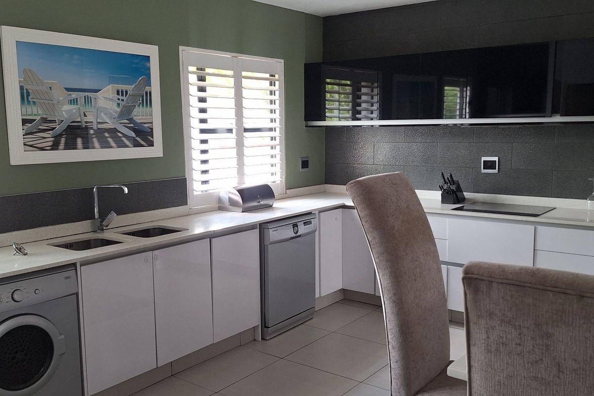 Modern kitchen featuring sleek white cabinetry, dark tiled backsplash, stone countertops, integrated appliances, and plantation shutters for natural light control.
