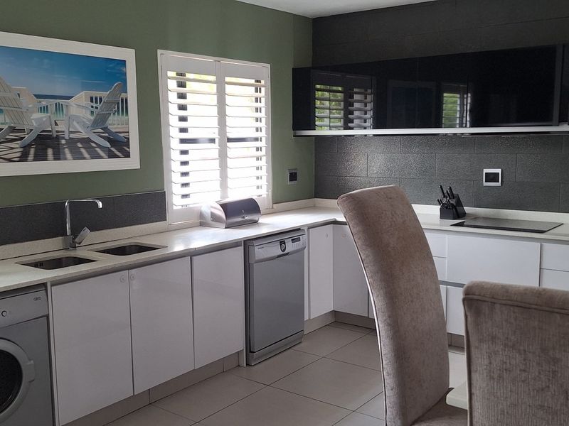 Modern kitchen featuring sleek white cabinetry, dark tiled backsplash, stone countertops, integrated appliances, and plantation shutters for natural light control.