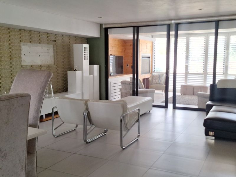 Spacious open-plan living area featuring large format floor tiles, a textured feature wall, and expansive sliding glass doors leading to an outdoor patio.