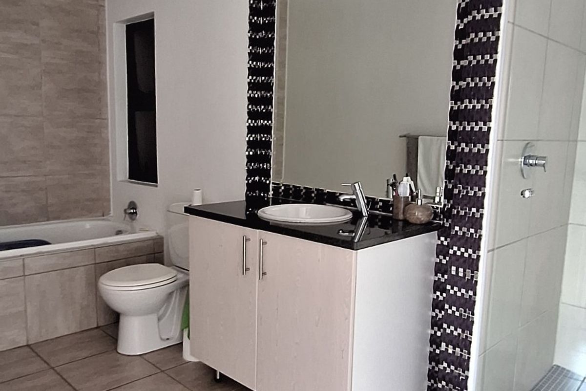 A functional bathroom featuring a built-in vanity with basin, a separate bathtub, and a glass-enclosed shower with neutral floor tiling.