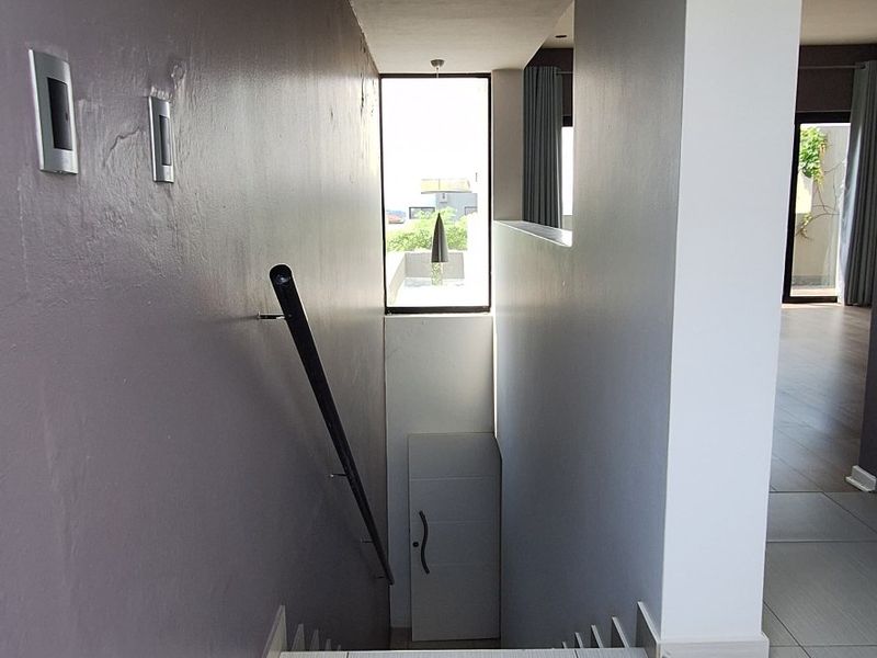 A bright, modern hallway featuring tiled flooring, a sleek staircase with a handrail, and recessed lighting, leading towards an open living area.