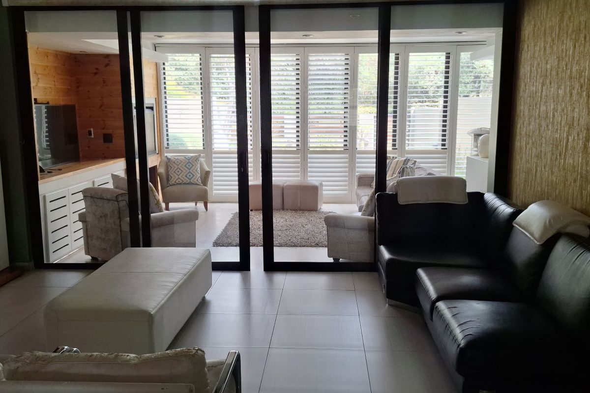 Spacious living area featuring large sliding glass doors with plantation shutters, tiled flooring, and recessed lighting, opening onto an adjacent sunroom space.