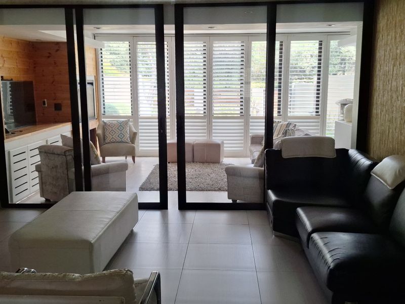 Spacious living area featuring large sliding glass doors with plantation shutters, tiled flooring, and recessed lighting, opening onto an adjacent sunroom space.