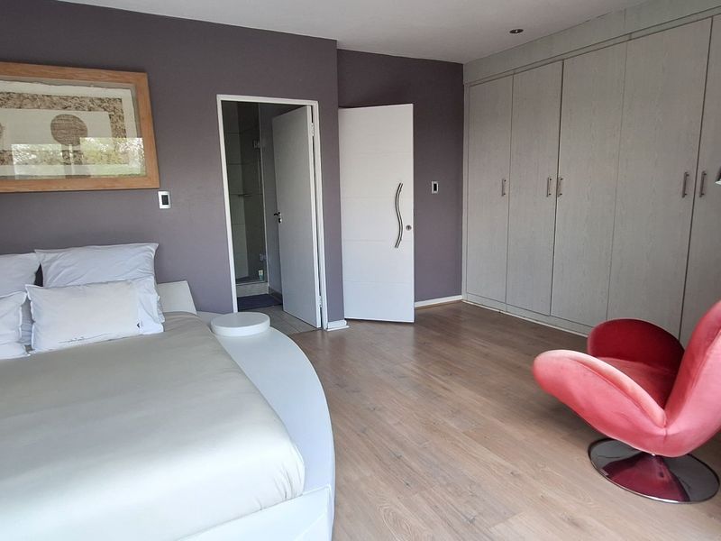 Spacious bedroom featuring laminate flooring, extensive built-in cupboards, and direct access to an en-suite bathroom.