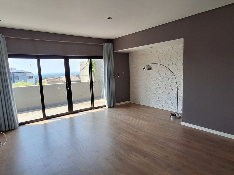 Spacious living room featuring laminate flooring, a textured feature wall, and large sliding glass doors that open to an outdoor balcony area.
