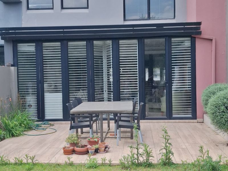 Rear view of a modern multi-story home featuring a timber deck, large aluminium stacker doors, and a private garden area.