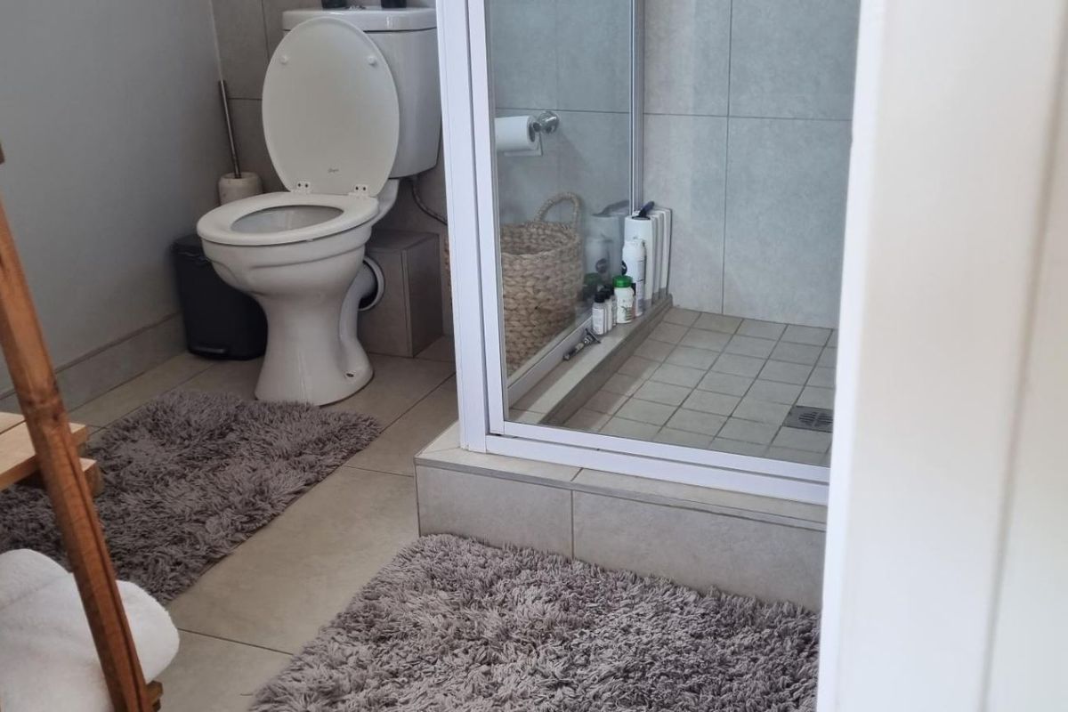 A functional bathroom featuring a toilet and a glass-enclosed shower with neutral wall and floor tiling.