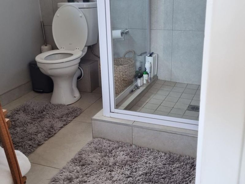 A functional bathroom featuring a toilet and a glass-enclosed shower with neutral wall and floor tiling.