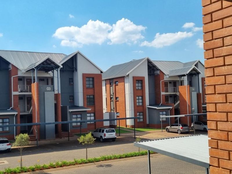 Exterior view of a modern multi-story apartment complex featuring brick and plaster facades, metal roofing, and covered parking bays.