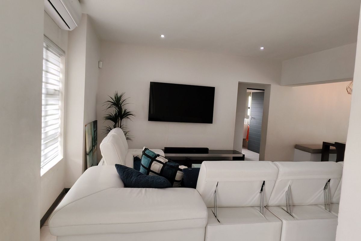A bright and modern living room featuring tiled flooring, recessed downlighting, and a wall-mounted air conditioning unit.