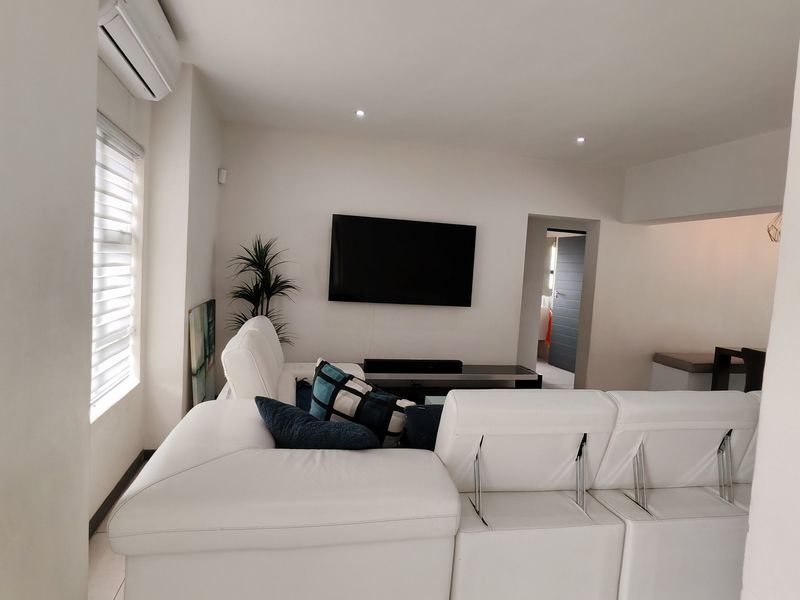 A bright and modern living room featuring tiled flooring, recessed downlighting, and a wall-mounted air conditioning unit.