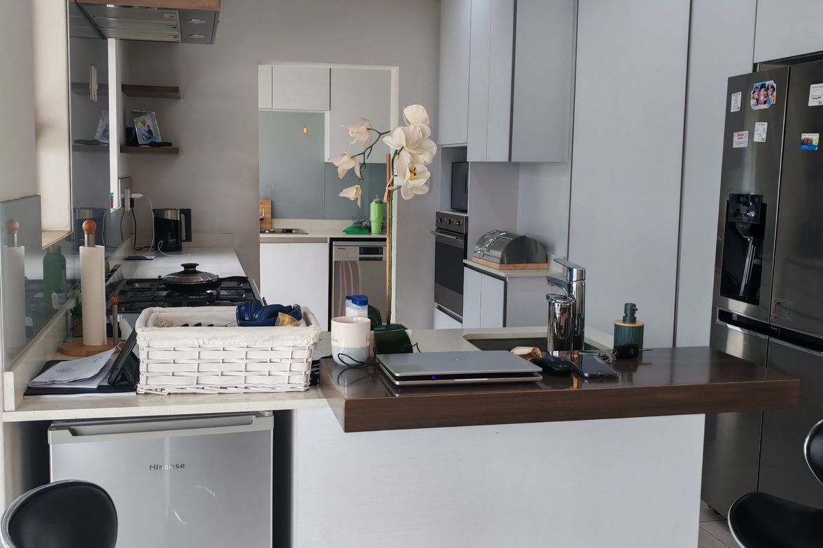 Modern kitchen featuring white cabinetry, a gas hob with extractor, built-in oven, and a breakfast bar with a dark wood countertop.