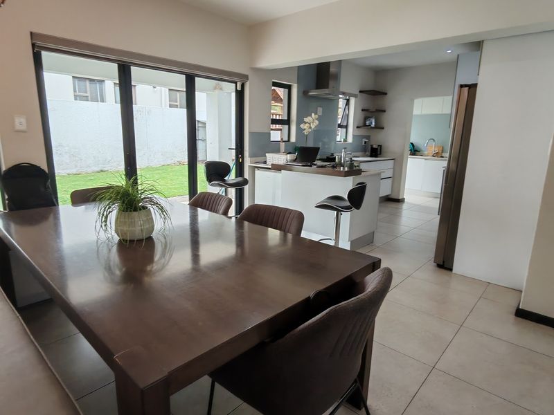 Open-plan dining and kitchen area featuring tiled floors, a central island, modern cabinetry, and large sliding doors leading to the garden.