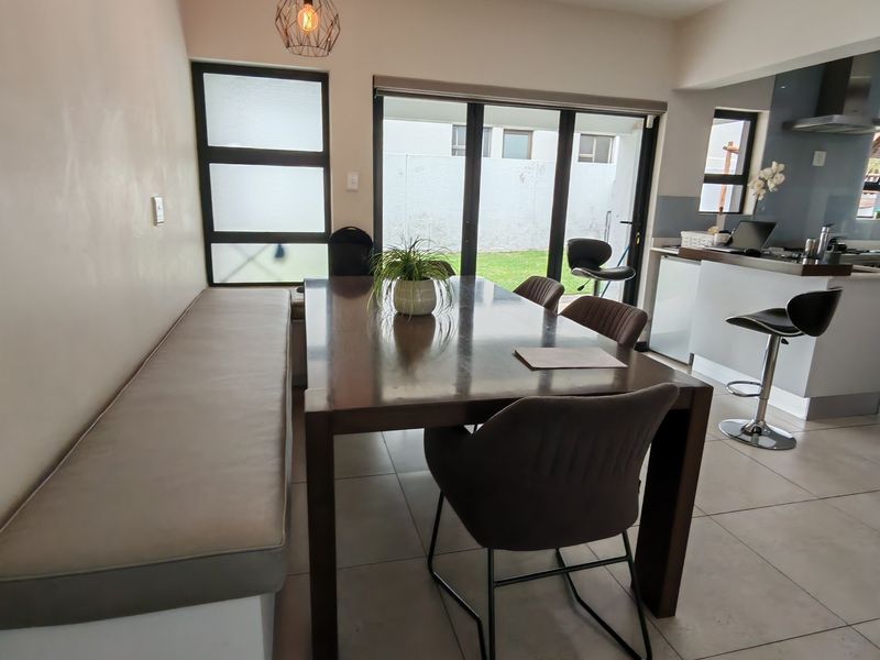Modern open-plan dining and kitchen area featuring tiled floors, built-in bench seating, and seamless access to the rear garden through sliding glass doors.