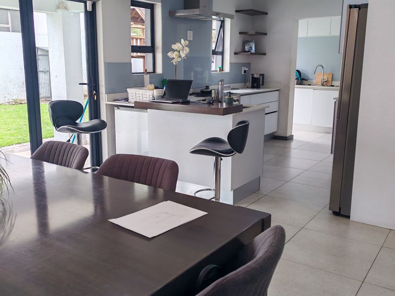 Modern open-plan kitchen and dining area featuring tiled floors, sleek cabinetry, a central island, and sliding doors leading to the garden.