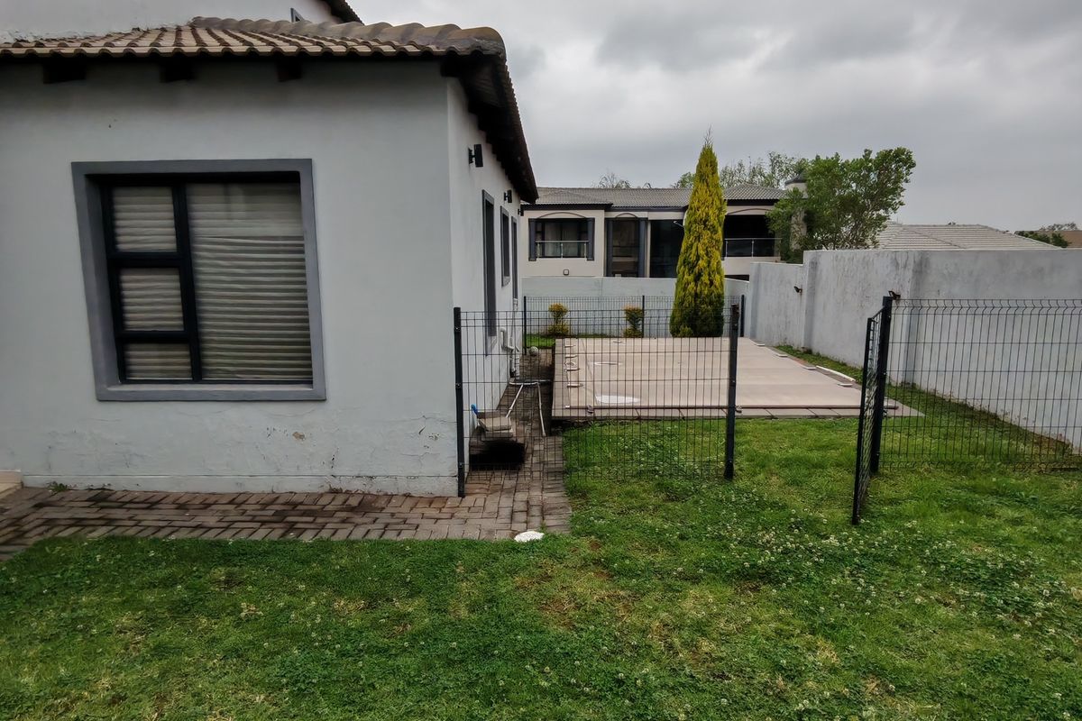 Rear exterior view of the property featuring a small lawn, paved walkway, perimeter fencing, and a covered swimming pool area.