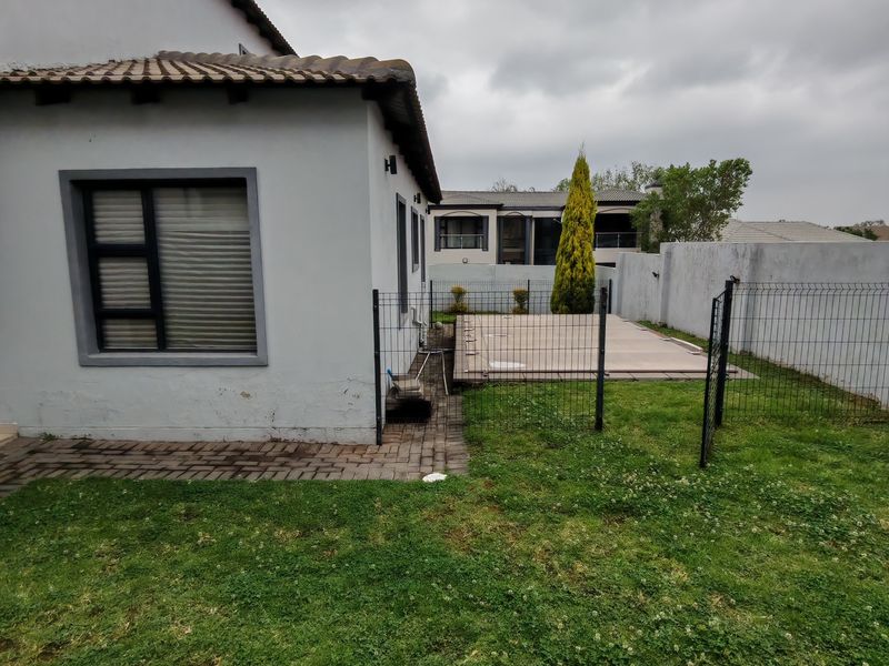 Rear exterior view of the property featuring a small lawn, paved walkway, perimeter fencing, and a covered swimming pool area.