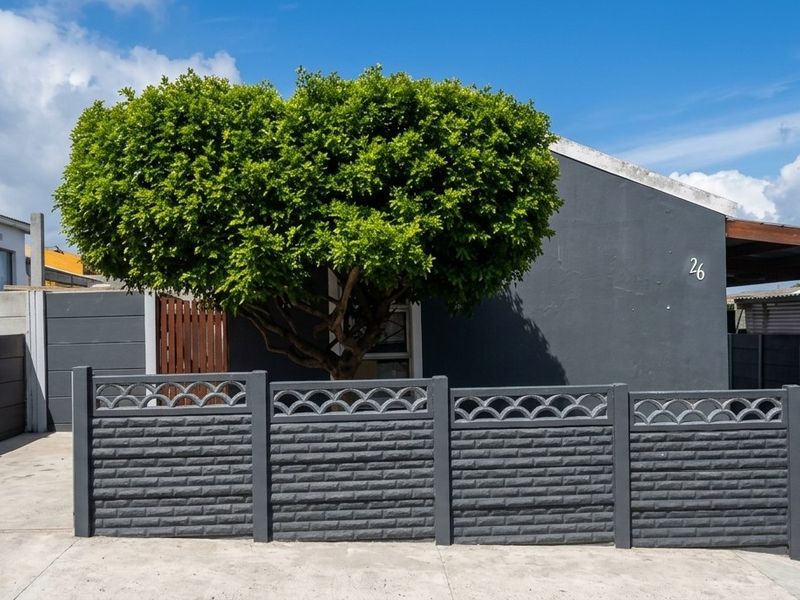 Front view of a residential property featuring a modern grey facade, a secure precast boundary wall, a metal driveway gate, and a covered carport area.