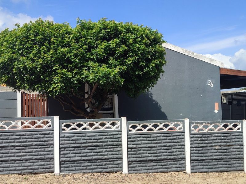 Front view of the property featuring a grey painted facade, a precast concrete boundary wall, and a covered carport area.