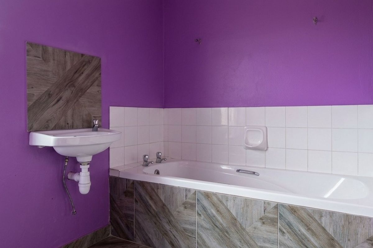 A bathroom featuring a built-in bathtub with tiled apron and a wall-mounted basin, finished with bold purple wall paint.