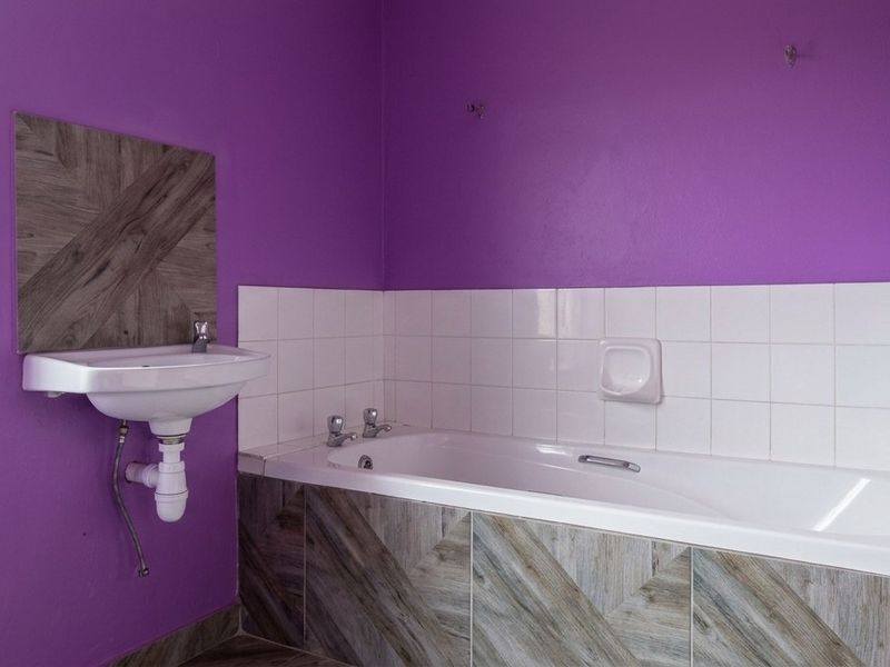 A bathroom featuring a built-in bathtub with tiled apron and a wall-mounted basin, finished with bold purple wall paint.