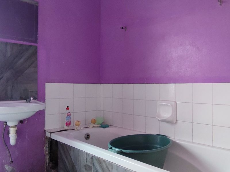 A dated bathroom featuring a wall-mounted basin and a built-in bathtub with missing side paneling, requiring renovation and cosmetic updates.