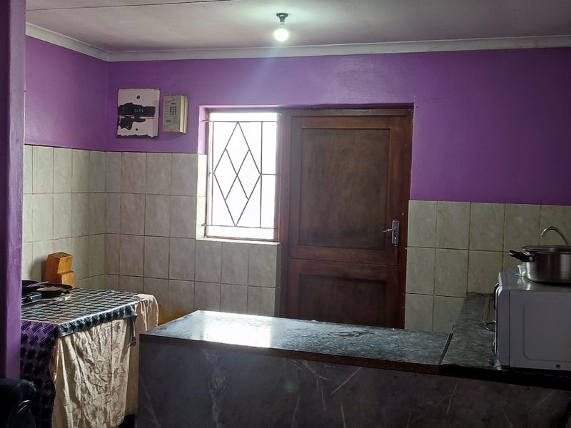 A functional kitchen area featuring tiled splashbacks, a built-in counter, and direct access to the exterior via a timber door with security gate.