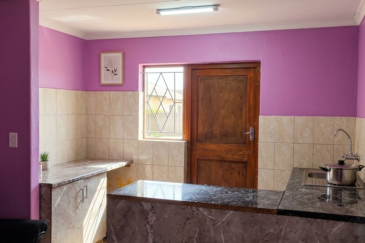 A functional kitchen featuring marble-effect countertops, tiled splashbacks, and direct access to the exterior via a wooden door.