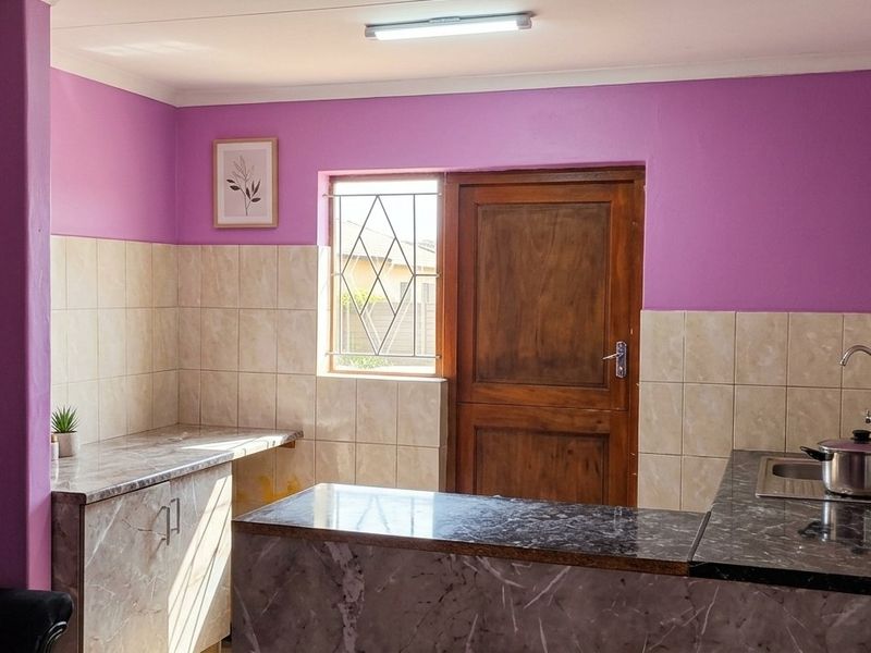 A functional kitchen featuring marble-effect countertops, tiled splashbacks, and direct access to the exterior via a wooden door.