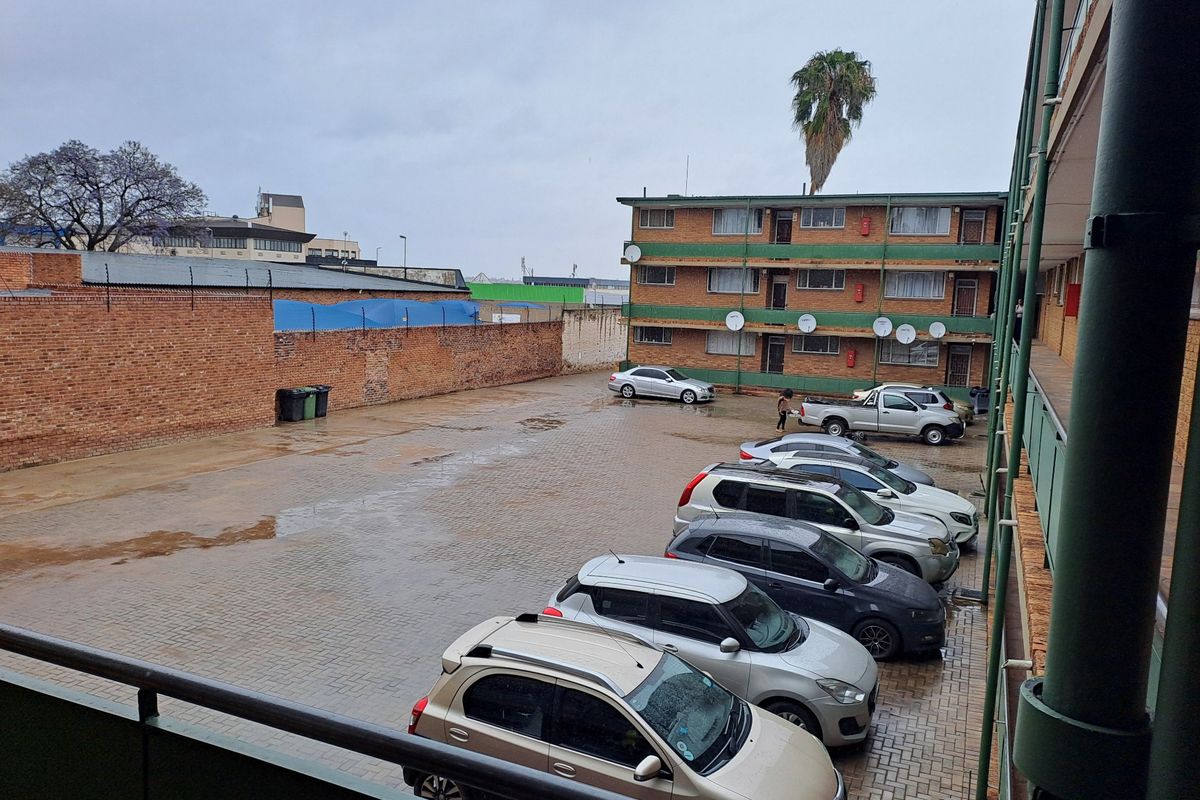 An elevated view of the apartment complex rear parking area featuring paved surfaces and a brick boundary wall.