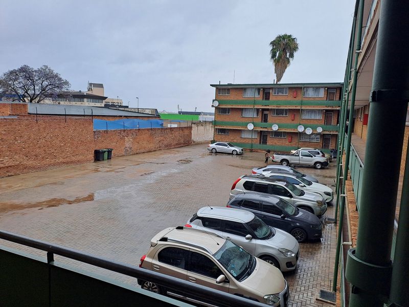 An elevated view of the apartment complex rear parking area featuring paved surfaces and a brick boundary wall.