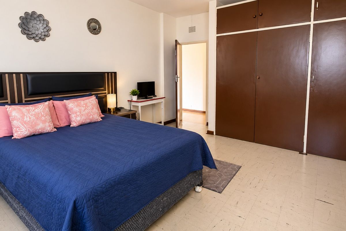 A bedroom featuring built-in cupboards and tiled flooring, offering a functional space with potential for cosmetic updates.