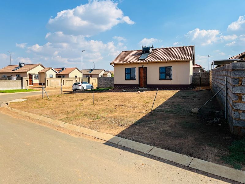 Front view of a detached house featuring a tiled roof, solar water heater, and a large, open, unlandscaped yard area.