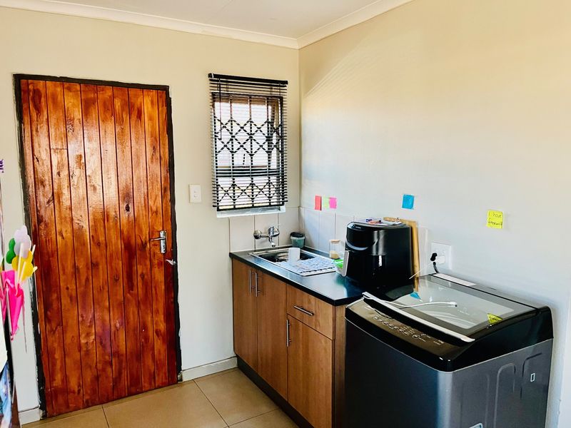 A functional scullery area featuring built-in cabinetry, a stainless steel sink, tiled splashback, and a secure window with a fitted security gate.
