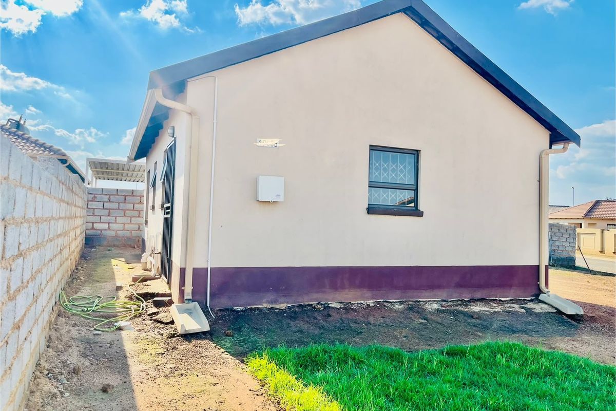 Rear view of the property showing the exterior wall, security gate, and basic boundary walling with an unfinished garden area.