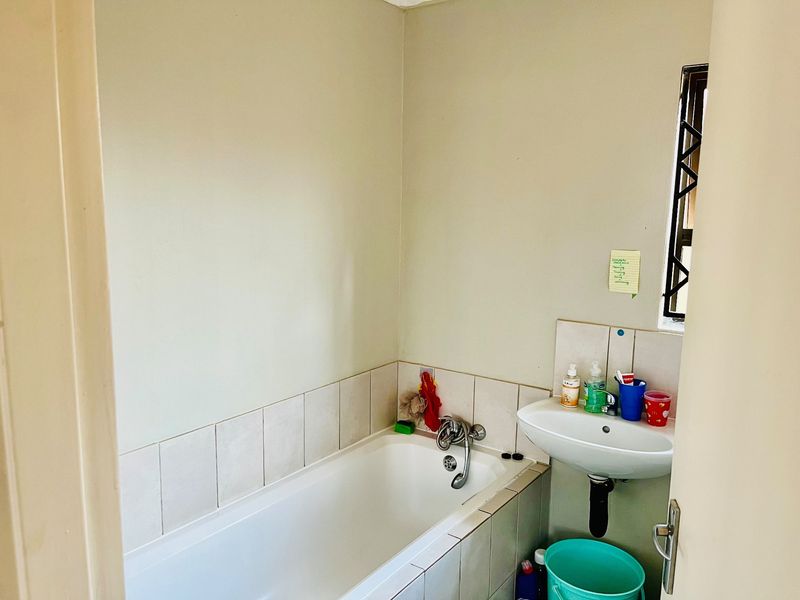 A functional bathroom featuring a standard bathtub, wall-mounted basin, and tiled splashback, providing essential amenities in a compact layout.