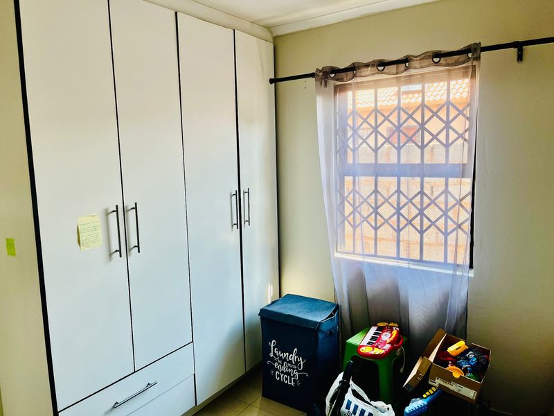 A bedroom featuring a large built-in wardrobe with white cabinetry and a window fitted with a security gate.