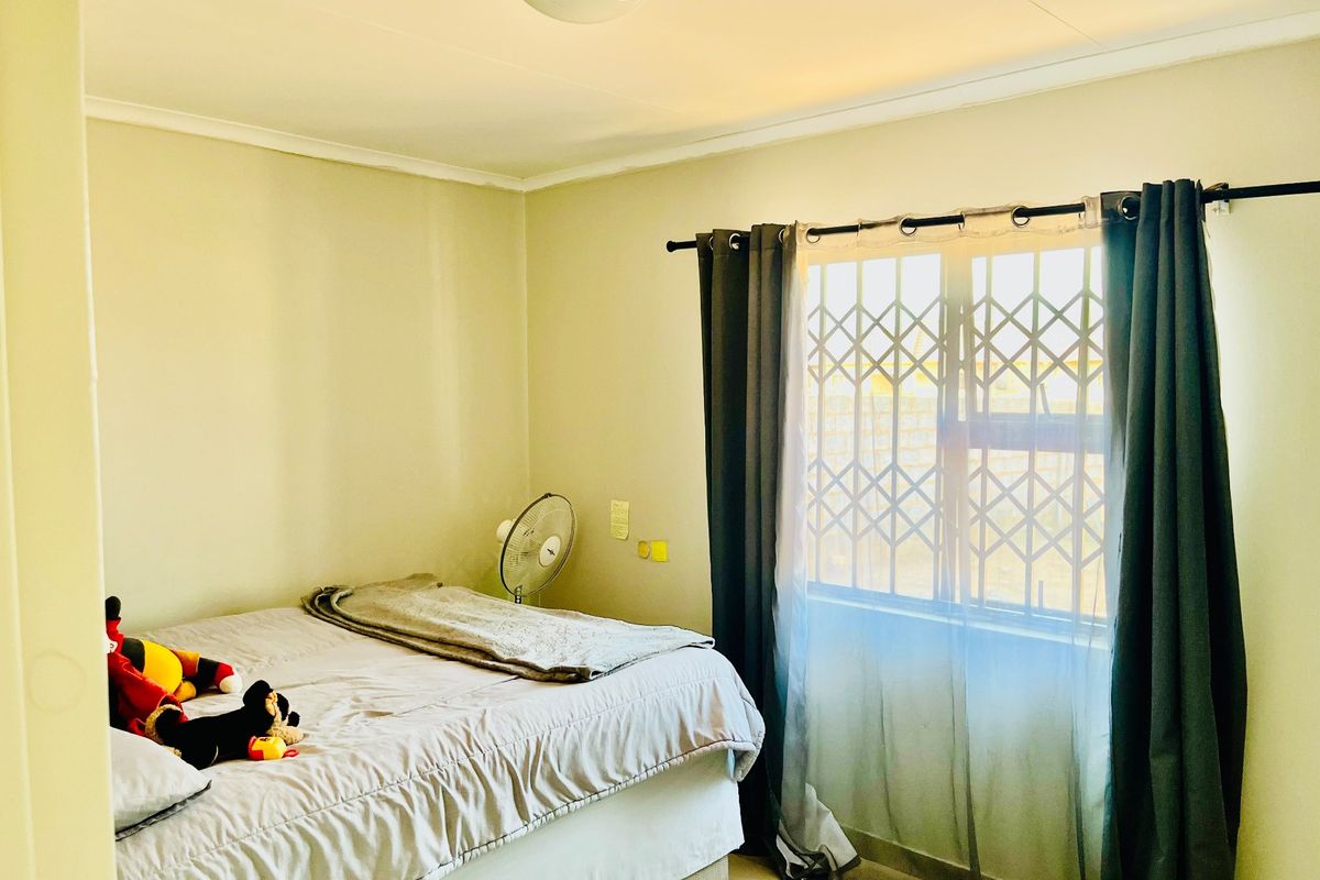 A functional bedroom featuring tiled flooring, a window with a security gate, and a central ceiling light fixture.