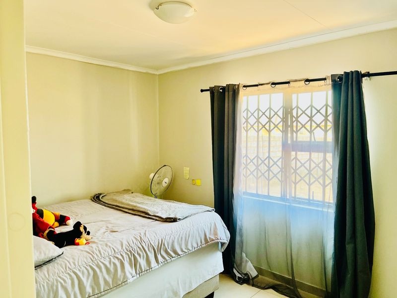 A functional bedroom featuring tiled flooring, a window with a security gate, and a central ceiling light fixture.