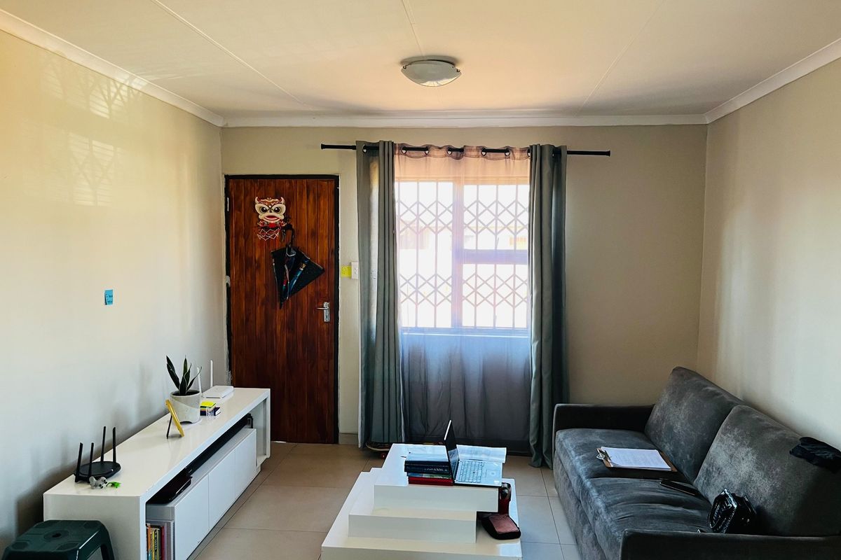 A functional living room featuring tiled flooring, a window with a security gate, and a standard ceiling light fixture.