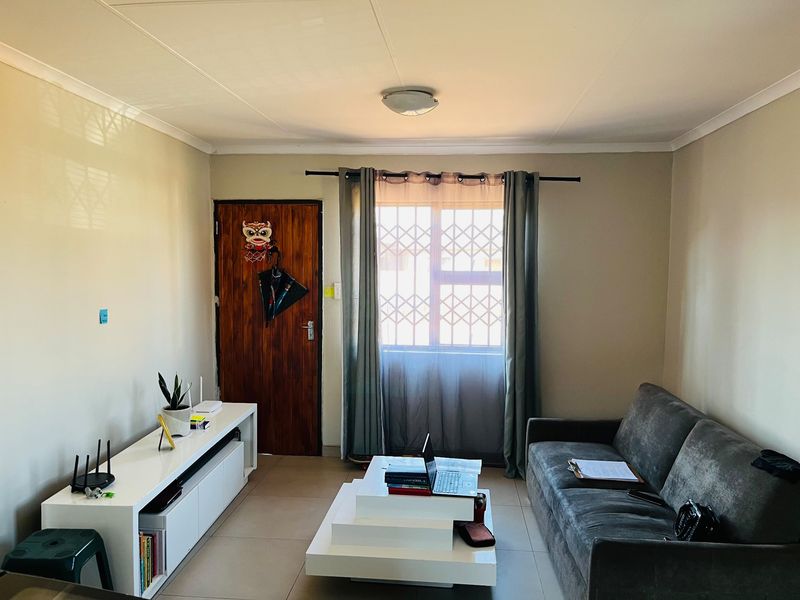A functional living room featuring tiled flooring, a window with a security gate, and a standard ceiling light fixture.