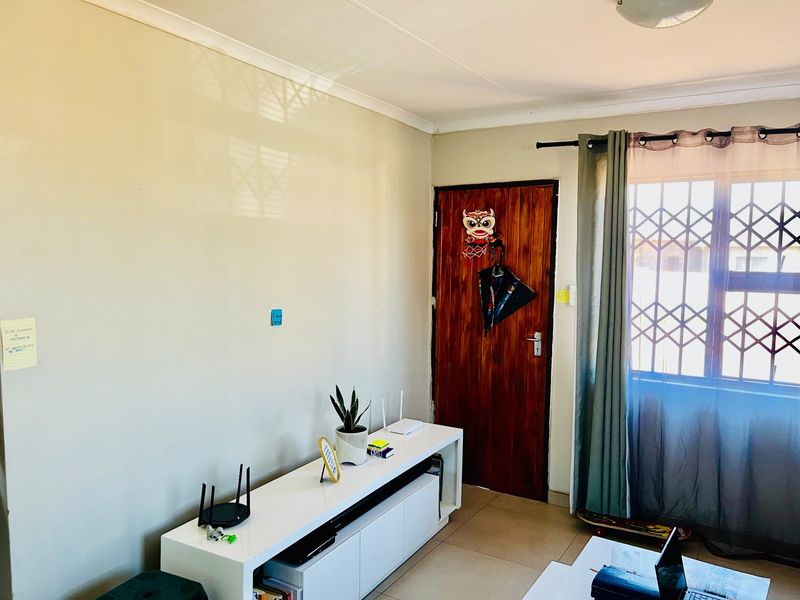 A living room area featuring tiled flooring, a wooden door with security gate, and a window with security bars.
