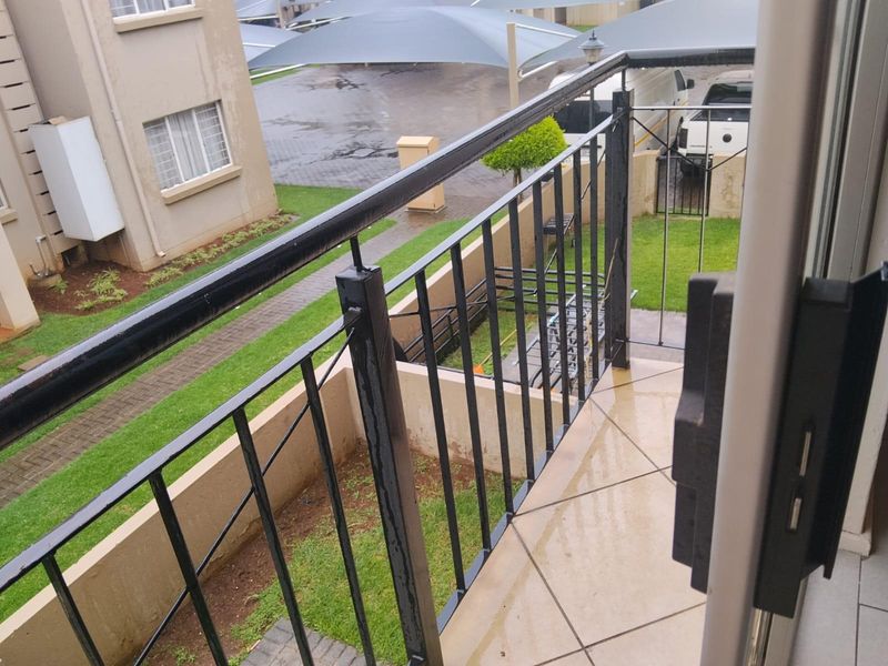 A ground-floor balcony featuring tiled flooring and a black metal balustrade, overlooking the complex grounds and parking area.