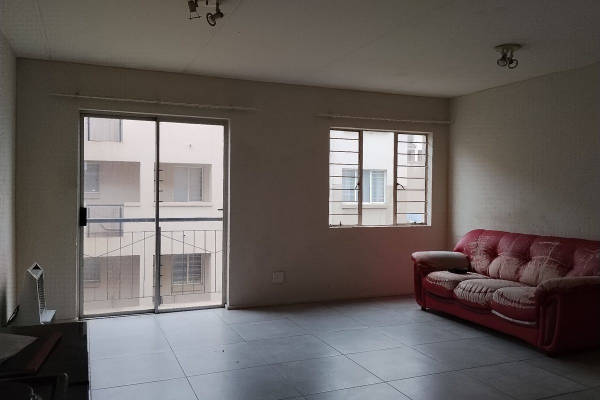 A living room featuring tiled flooring, a sliding glass door with security bars, and ceiling-mounted lighting, offering a blank canvas for renovation.